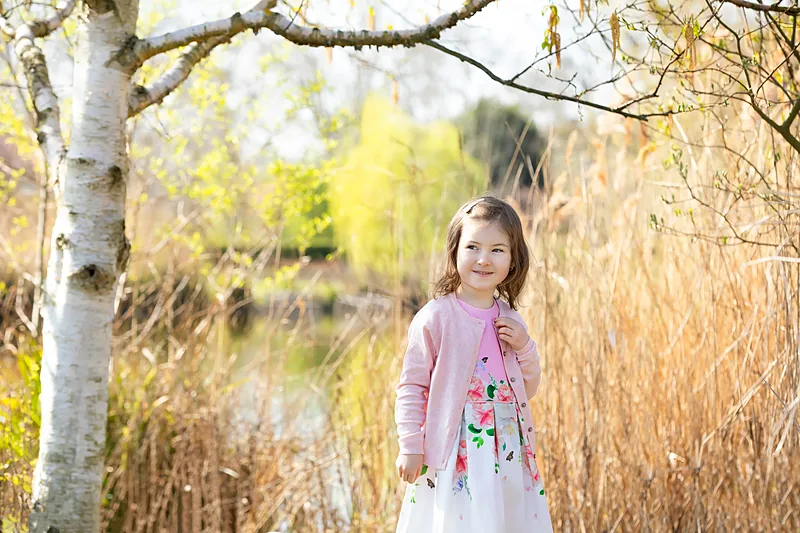 Girl in a pink top standing beside a birch tree by a lake