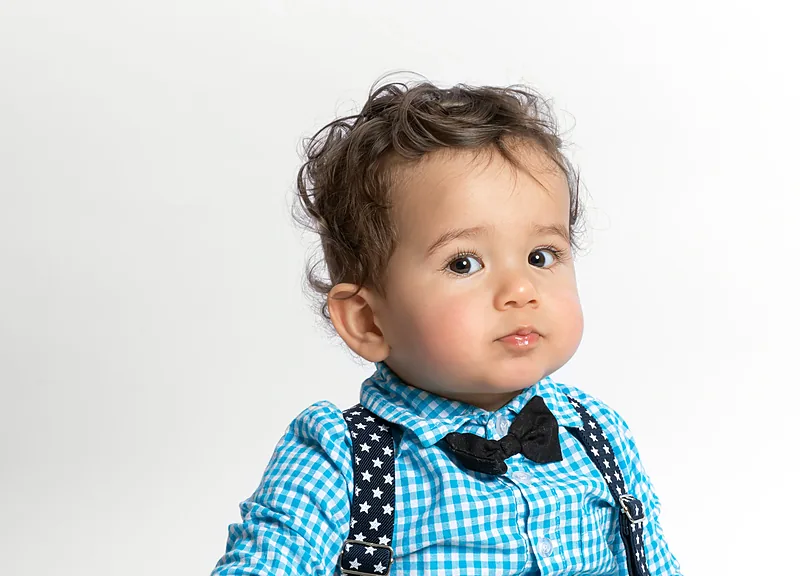 Toddler boy in a blue checked shirt and bow tie, white background