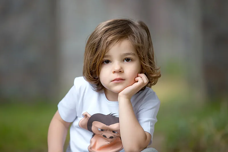 Young child in a white t-shirt resting their chin on one hand, outdoors