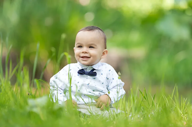 Toddler boy in a bow tie and braces standing in long grass