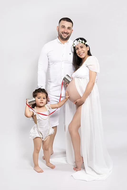 Expectant couple in white with their young son, studio portrait