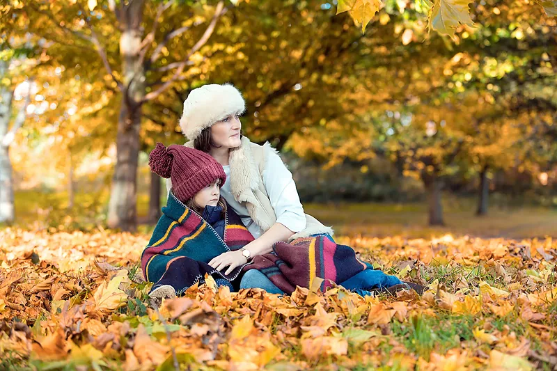 Family sitting among autumn leaves under golden trees
