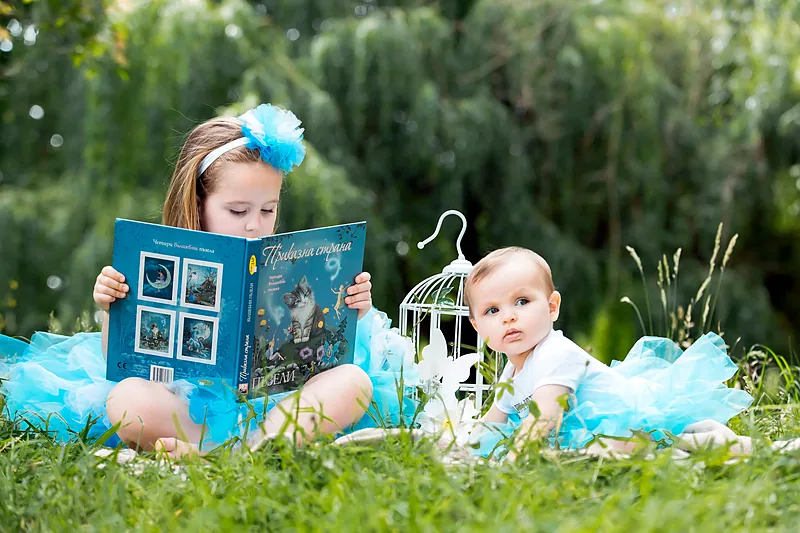 Two children in blue on the grass with a small photo frame and a birdcage