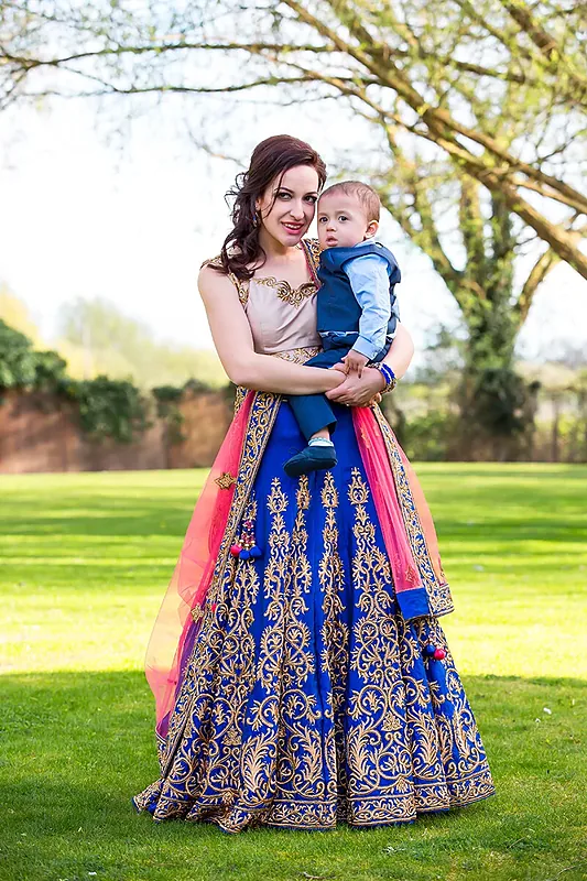Mother in a blue and pink embroidered dress holding a toddler on a lawn