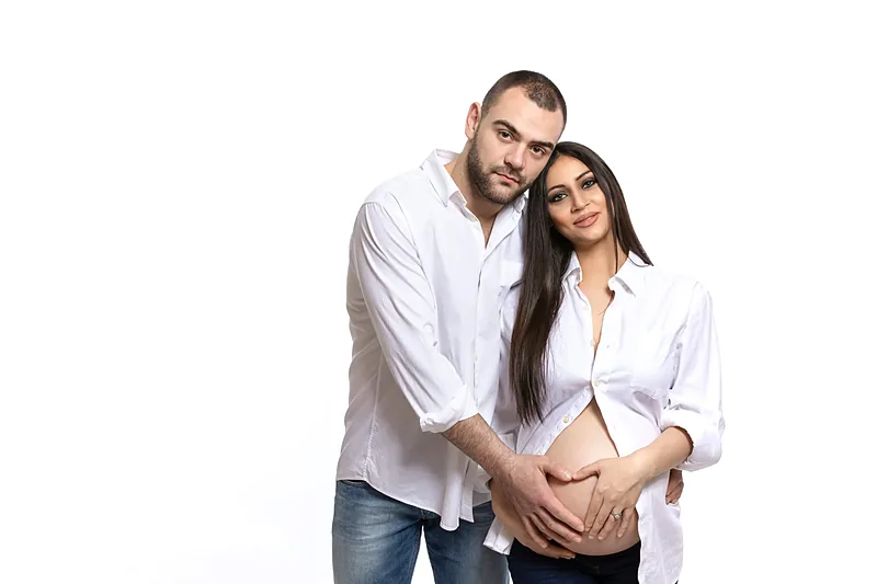 Expectant couple in white shirts, studio portrait on white
