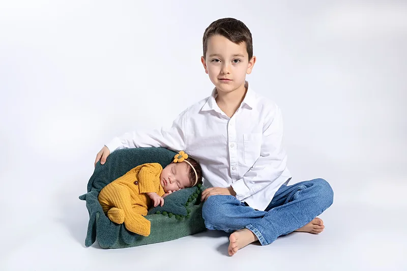 Boy sitting beside a newborn on a small green sofa