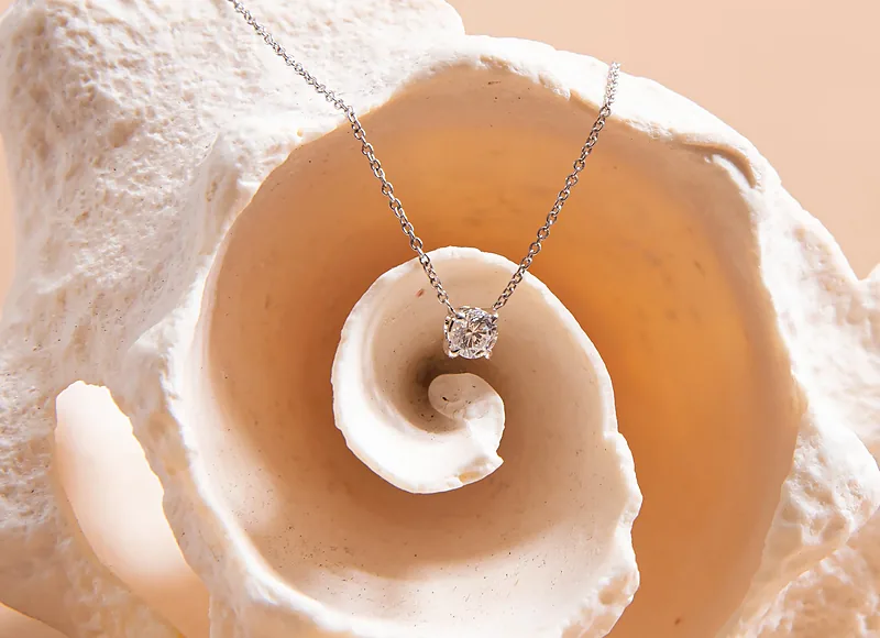 Diamond pendant on a chain resting on a white spiral shell