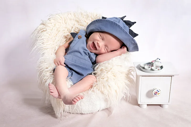 Newborn in a blue knitted outfit asleep in a tiny white armchair