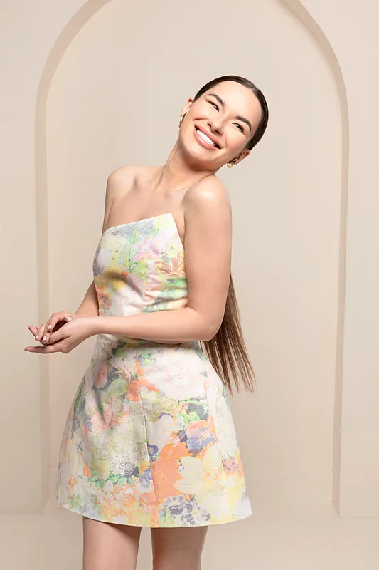 Woman in a floral mini dress posing in front of a cream arch backdrop