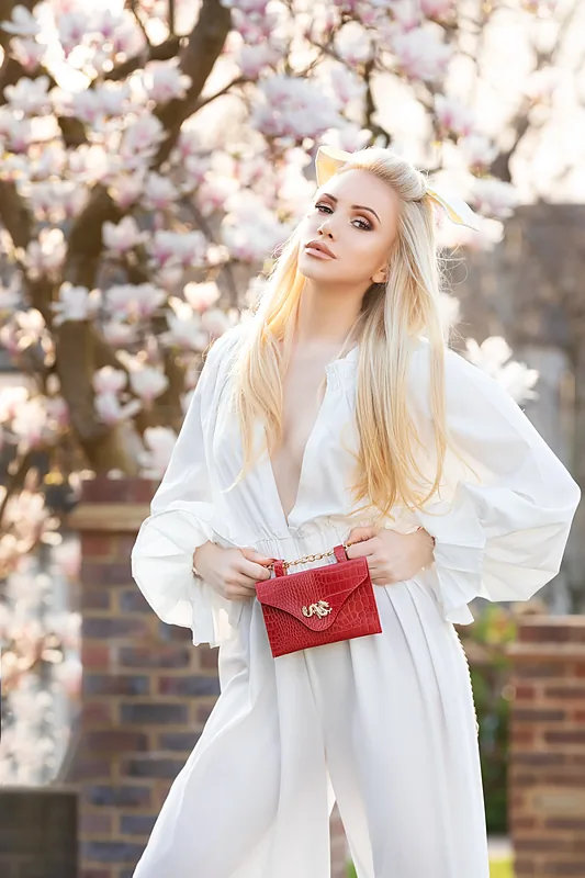 Woman in a white shirt holding a red bag under a blossom tree