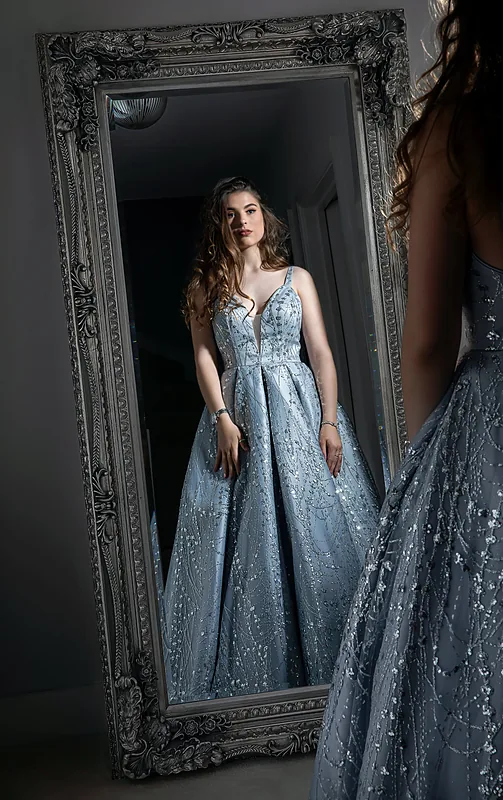 Woman in a pale blue gown reflected in a large ornate mirror