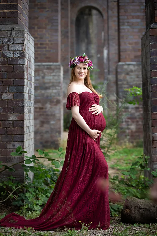 Expectant mother in a long burgundy gown standing in an old brick archway