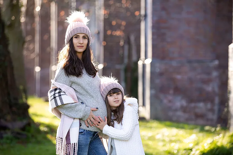 Expectant mother in a bobble hat with her young daughter in a park in winter