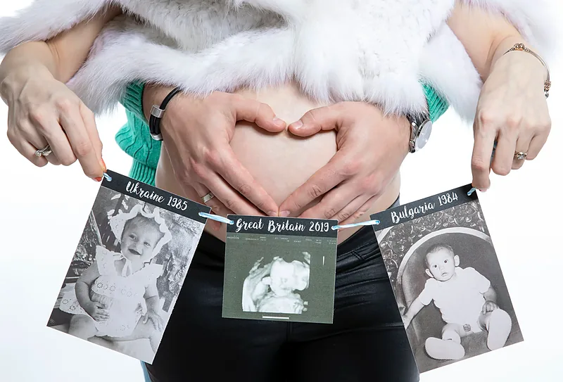 Close-up of a couple's hands making a heart shape on a bare bump, with ultrasound prints