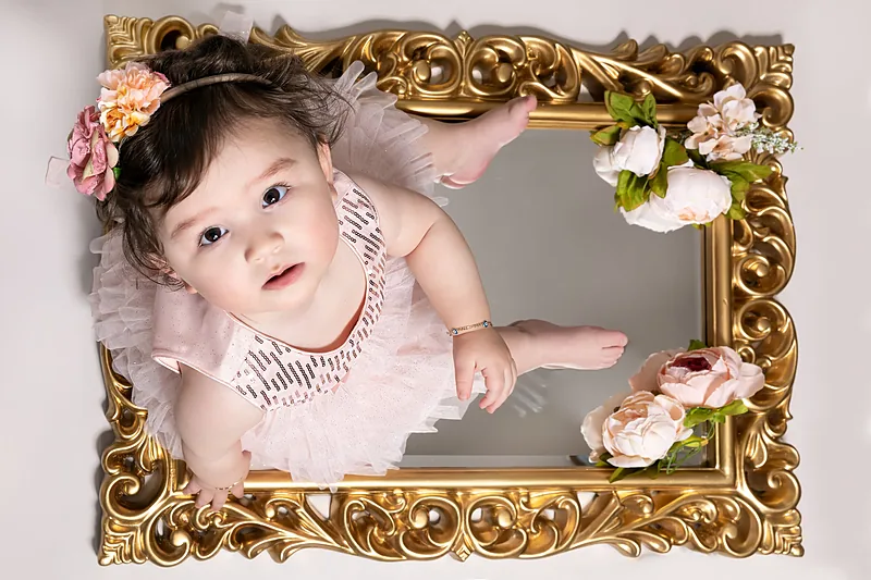 Baby with a flower headband lying inside an ornate gold picture frame