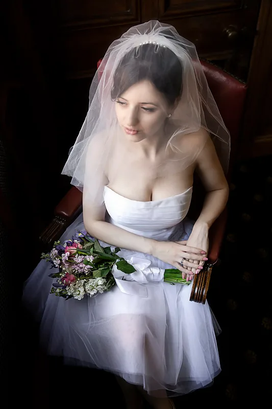 Bride in a short white dress and veil holding a bouquet, seated indoors