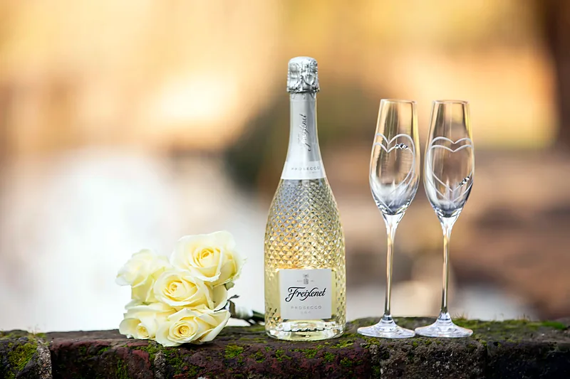 Bottle of sparkling wine with two glasses and pale roses on a wooden table