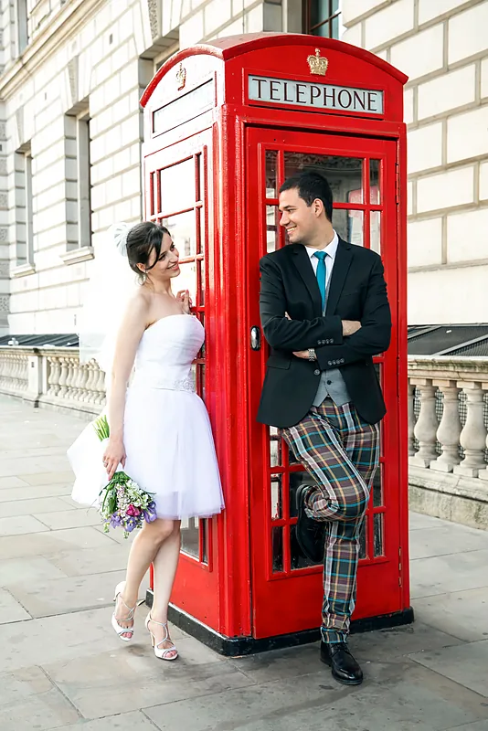 Bride and groom posing in a red London telephone box