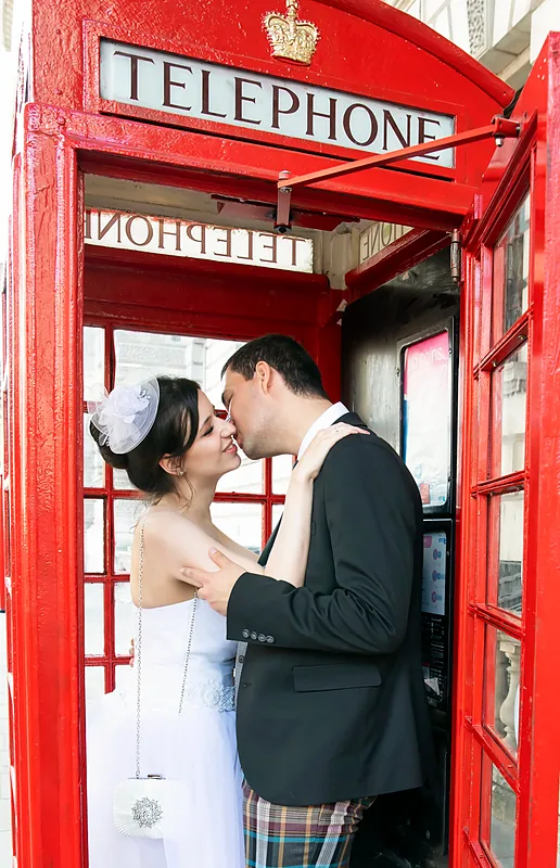 Bride and groom kissing inside a red telephone box