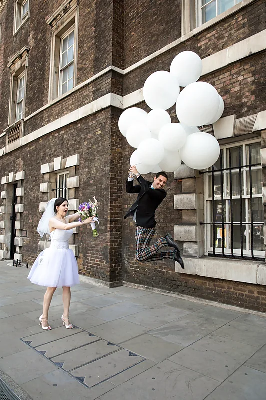 Bride and groom holding white balloons on a city street