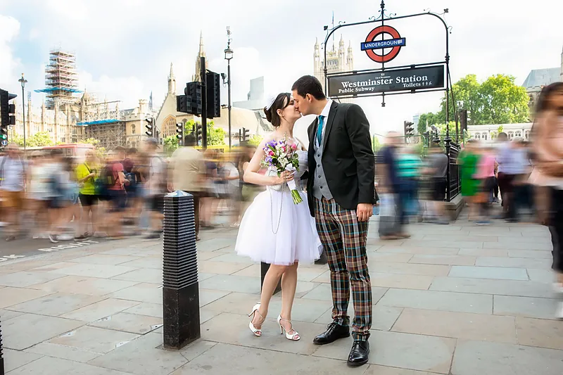 Bride and groom kissing beneath a London Underground sign on a busy street