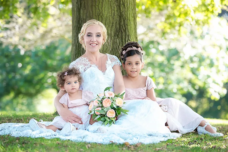 Bride seated on the grass beneath a tree with two flower girls
