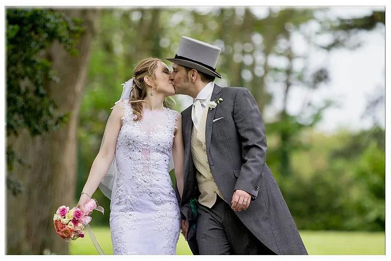 Bride and groom in a top hat kissing on a lawn