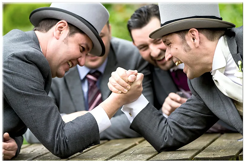 Groomsmen in top hats gathered around a table joking with the groom